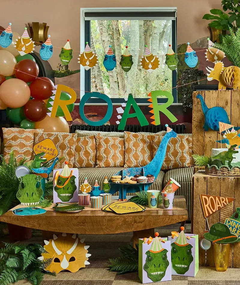 Dinosaur-themed party display with ROAR banner, dinosaur decorations, balloons, party tableware, gift bags, and prehistoric-themed party accessories. Dinosaur-themed party display with ROAR banner, dinosaur decorations, balloons, party tableware, gift bags, and prehistoric-themed party accessories.